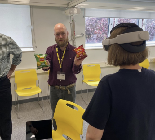 Learning designer Tim using packets of crisps with different colour bags to demonstrate the colour blindness setting in the VR app.